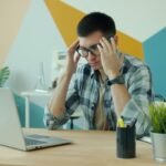 Man at a laptop touching his temples because of a headache